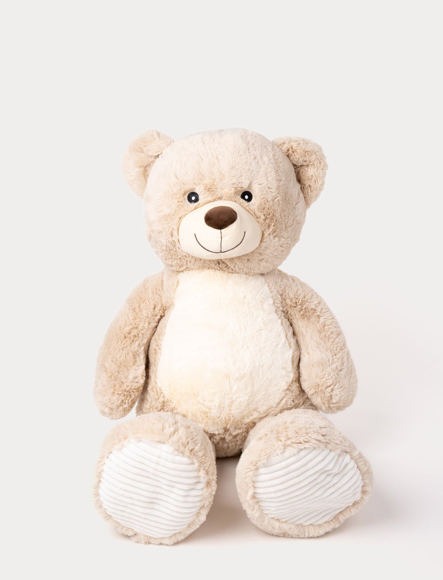 Soft beige teddy bear with a white belly, embroidered smile, and ribbed fabric on its paws.
