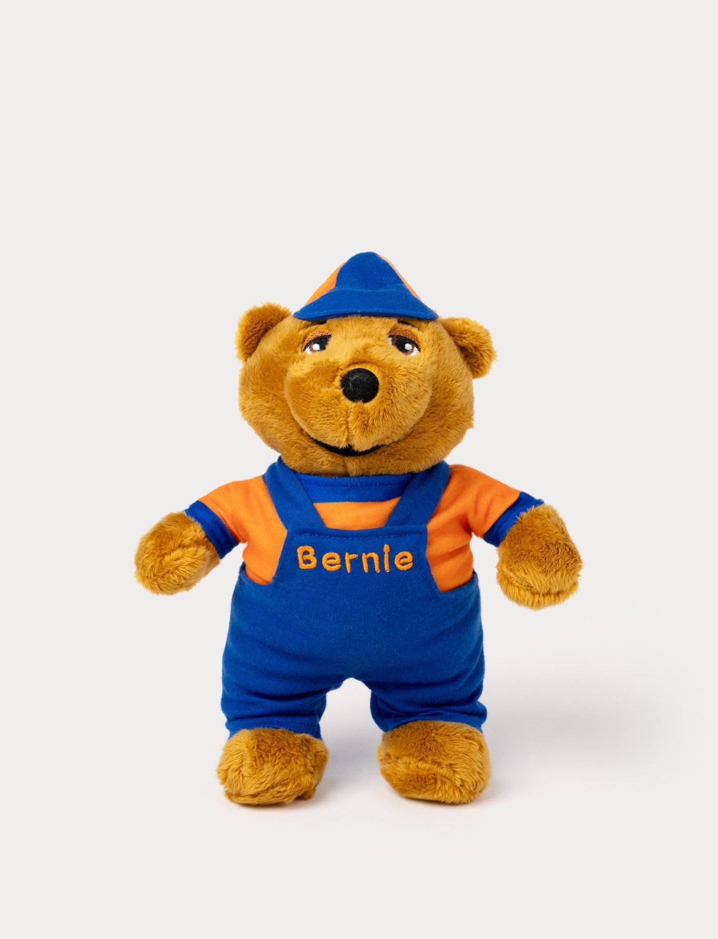 A plush toy of Bernie the bear wearing blue overalls and an orange shirt with his name embroidered.