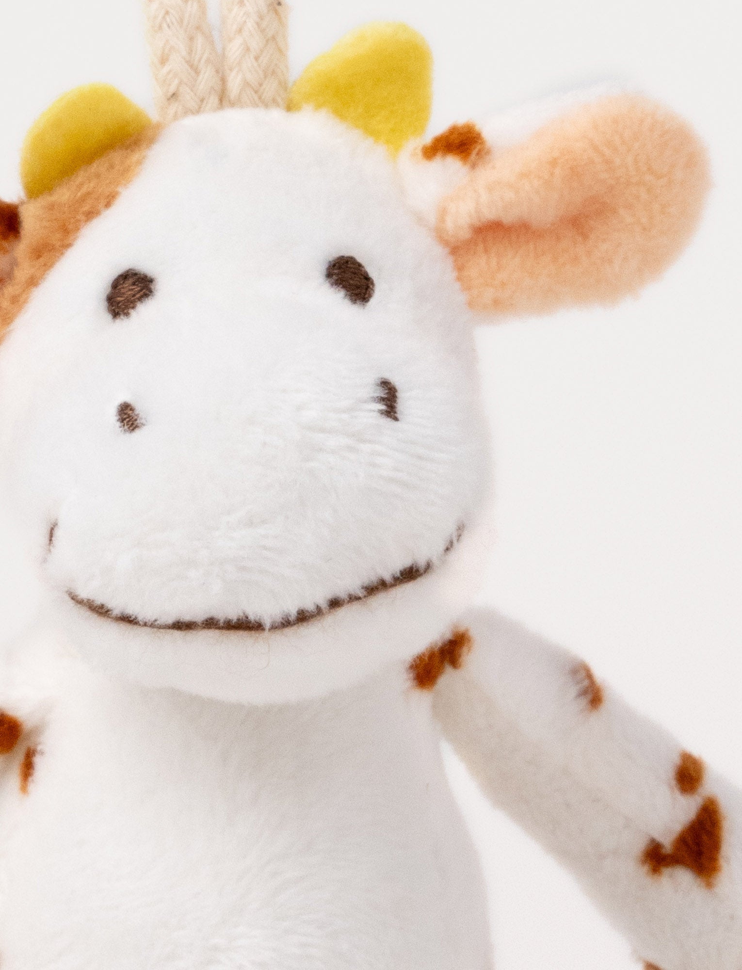  Image of A plush cow clip toy with a white body, brown spots, beige hooves, and a round bear-illustrated clip.