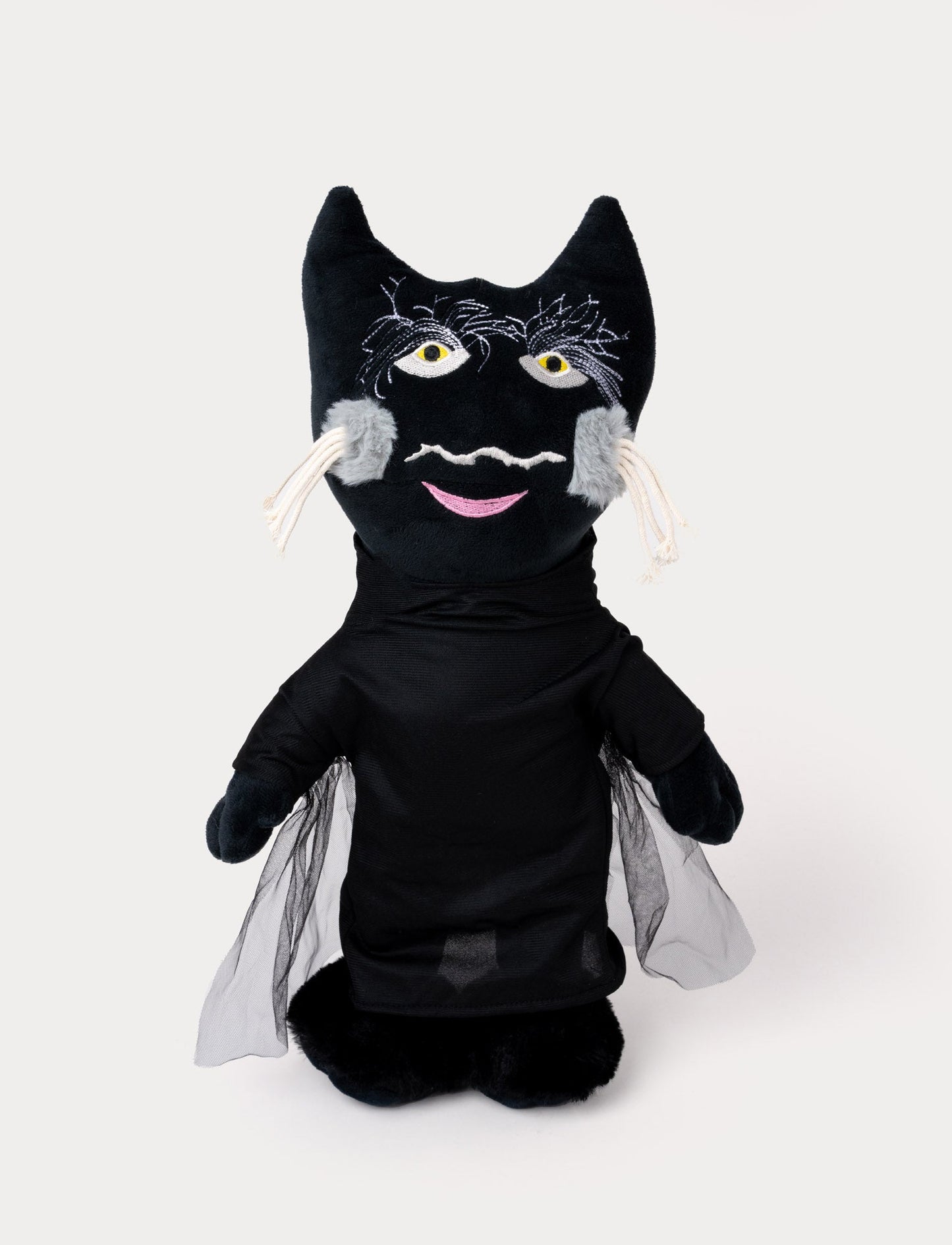 A plush toy of a black cat wearing a dark outfit with mesh cape details and embroidered facial features.