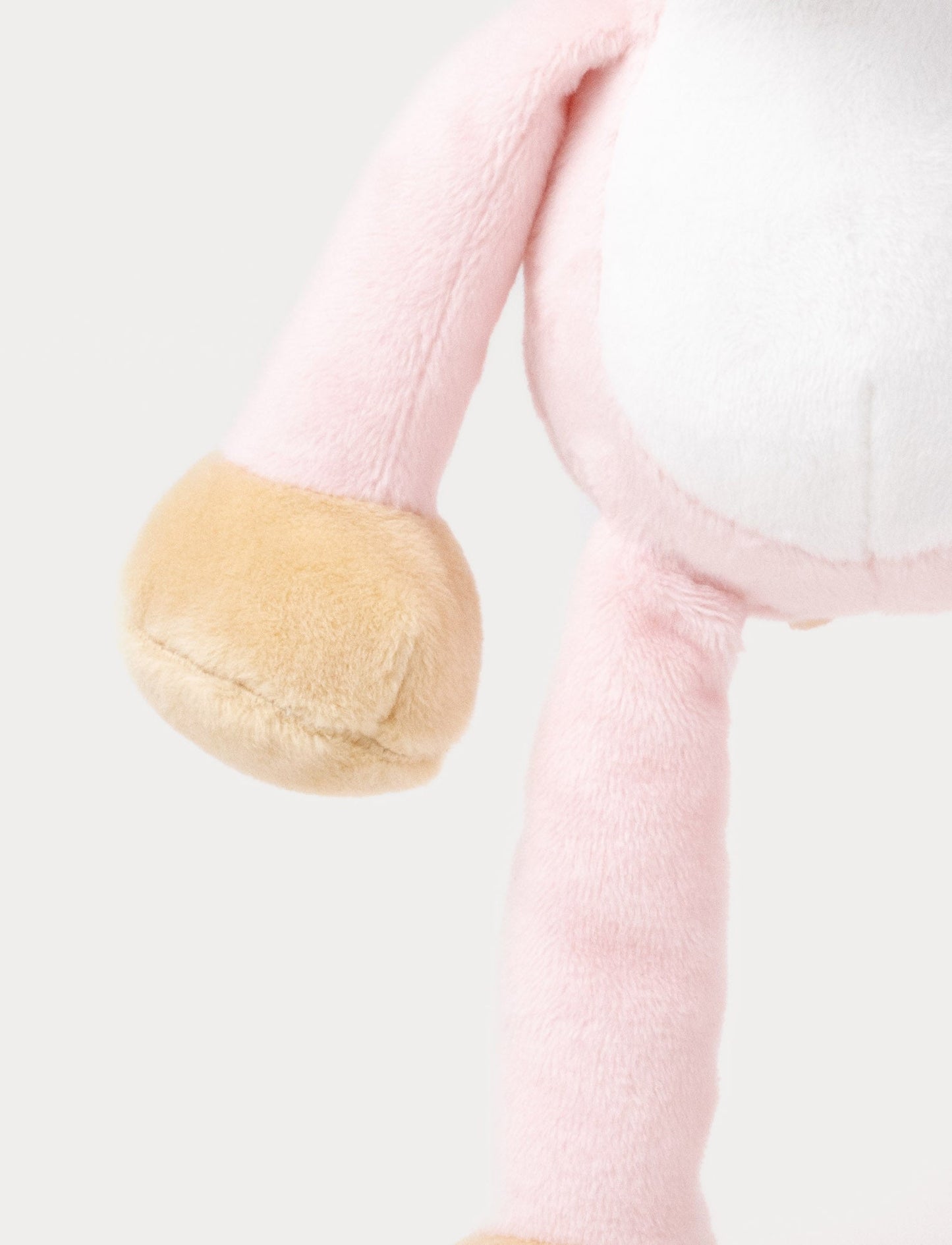 A plush pink cat music box toy with a white belly, beige paws, a stitched smiling face, and a fabric loop on top for hanging
