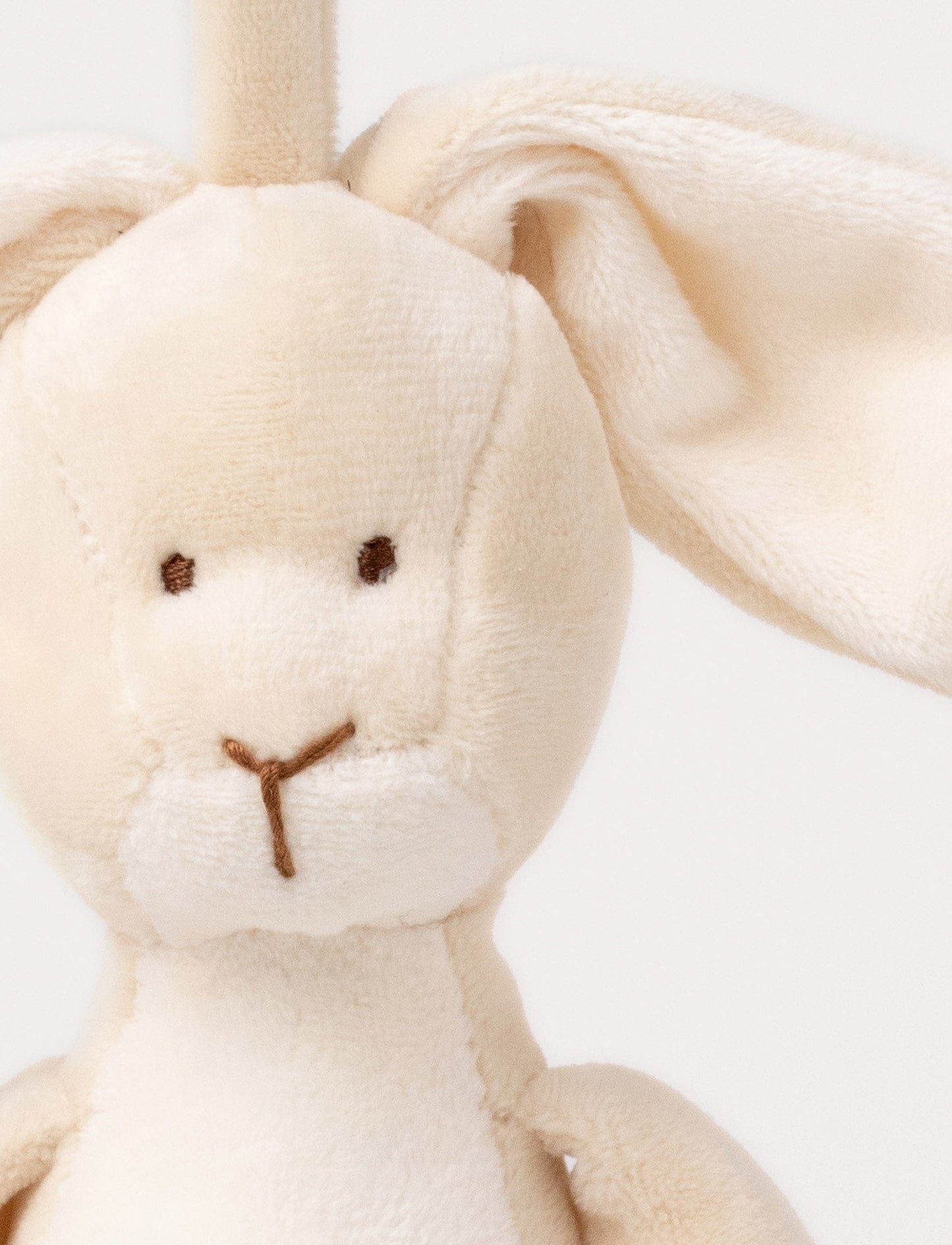 A plush beige bunny music box with floppy ears, a white belly, and a hanging loop.