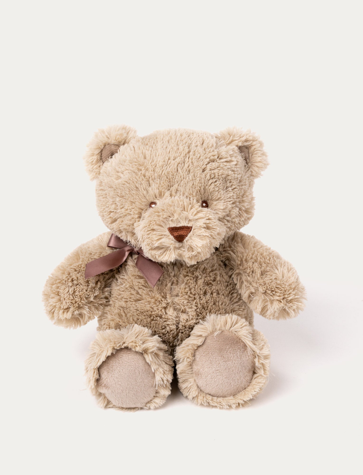  Image of Soft, light brown teddy bear with fluffy fur, a stitched brown nose, and a mauve ribbon tied around its neck.