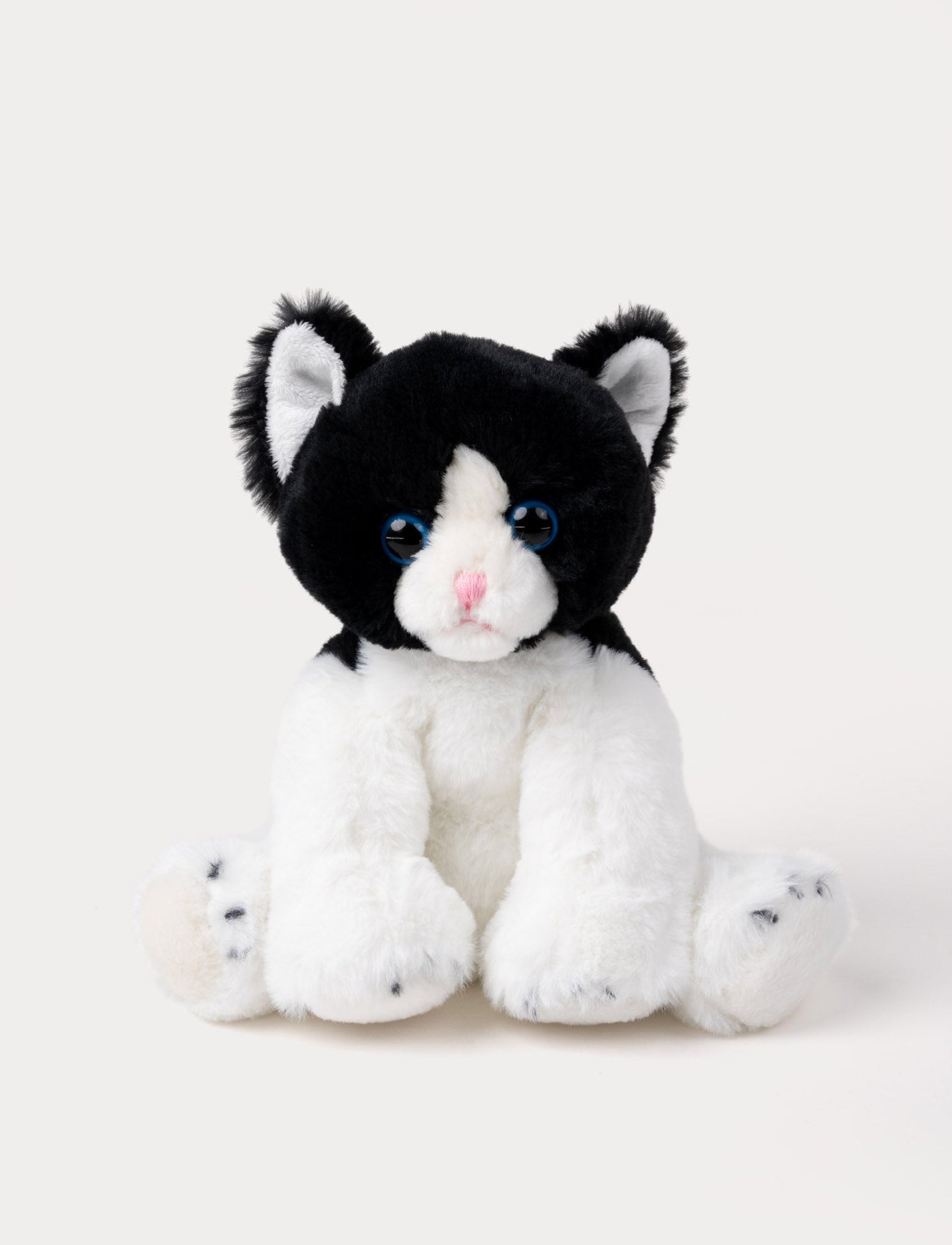 Soft black and white kitten plush with blue eyes, a pink nose, and white paws.