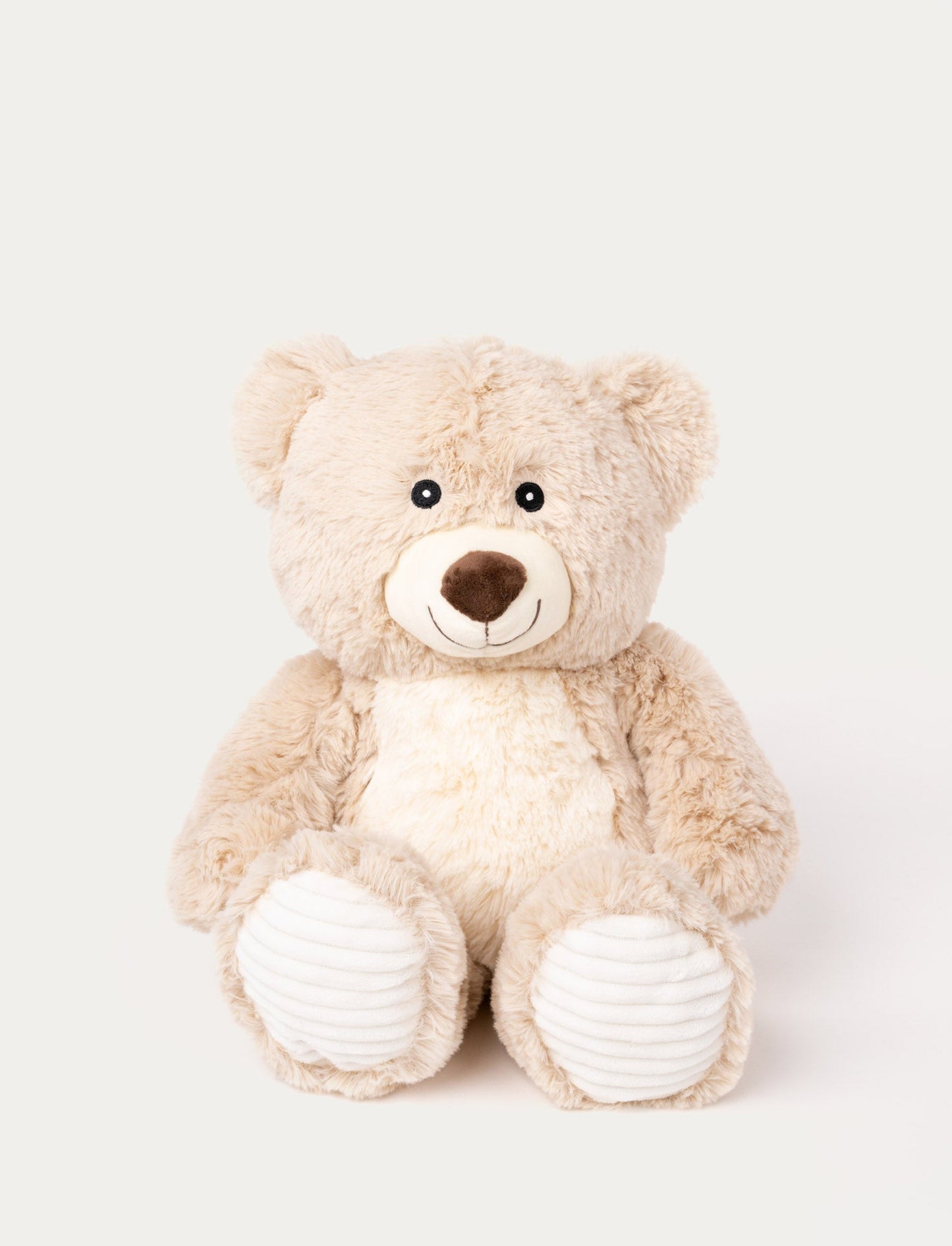 Soft beige teddy bear with a white belly, a stitched smile, and ribbed white fabric on its paws.