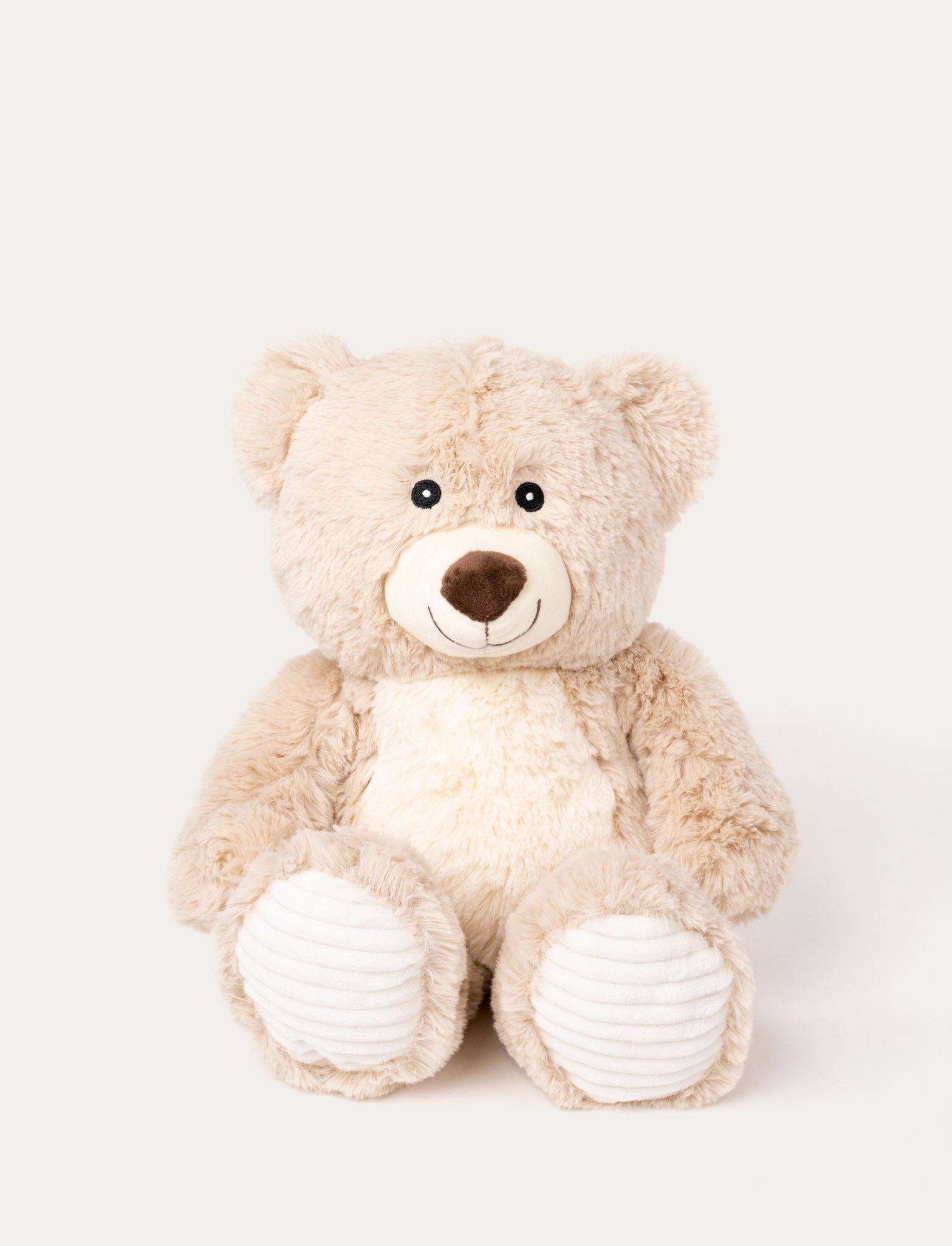  Image of Soft beige teddy bear with a white belly, a stitched smile, and ribbed white fabric on its paws.
