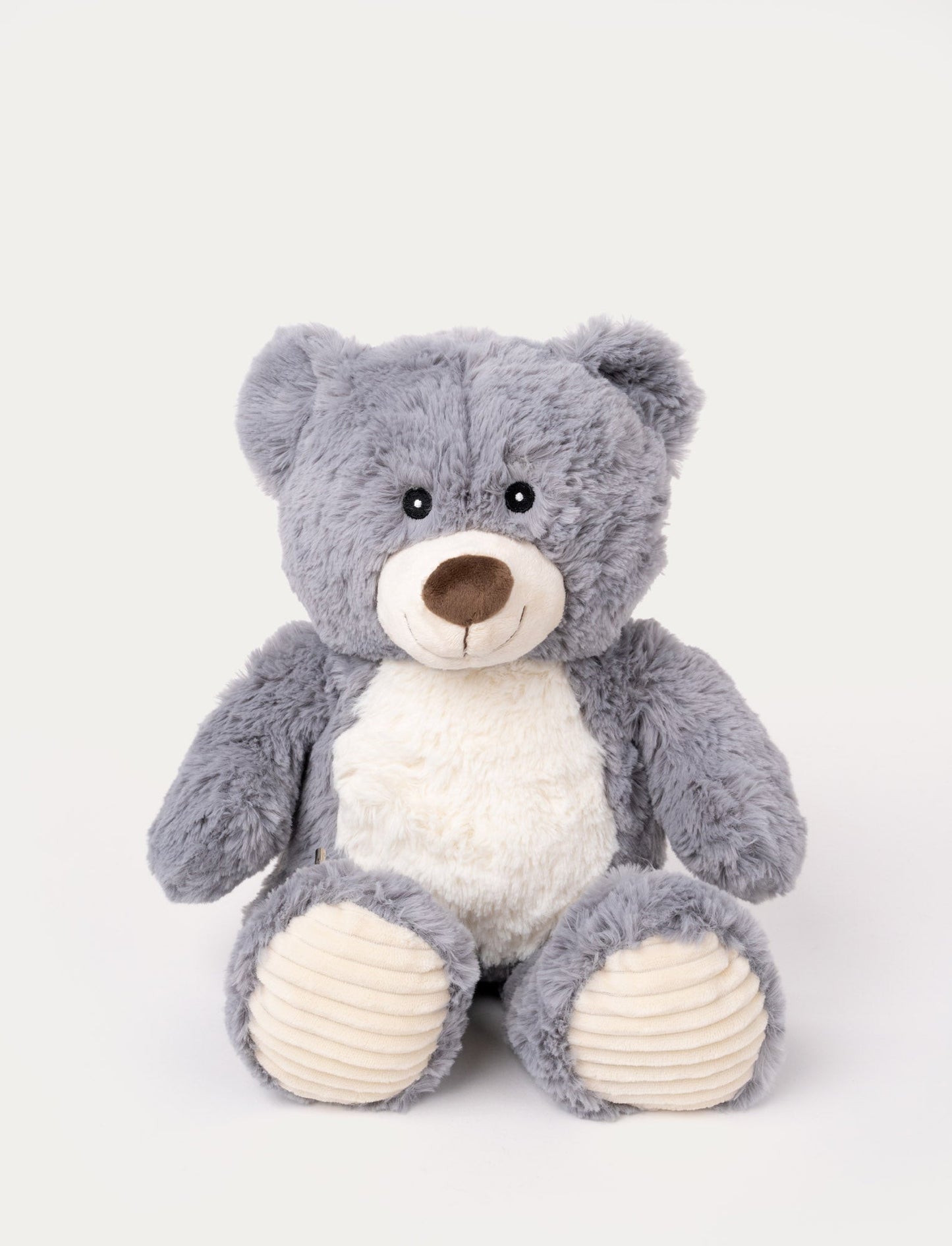 Soft grey teddy bear with a white belly, a stitched smile, and ribbed beige fabric on its paws.
