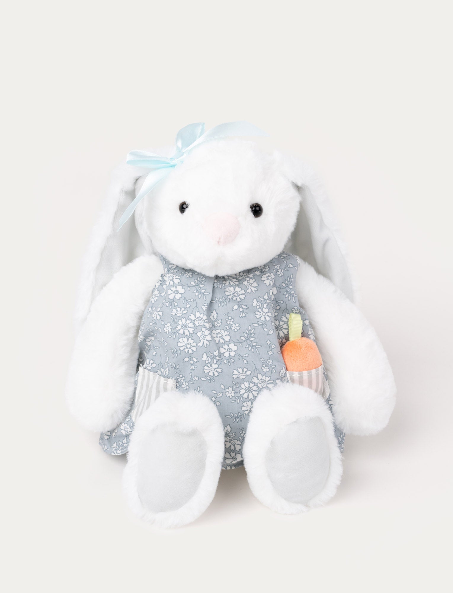  Image of Soft, white plush bunny with long floppy ears, wearing a blue floral dress with a pocket holding a small plush carrot.