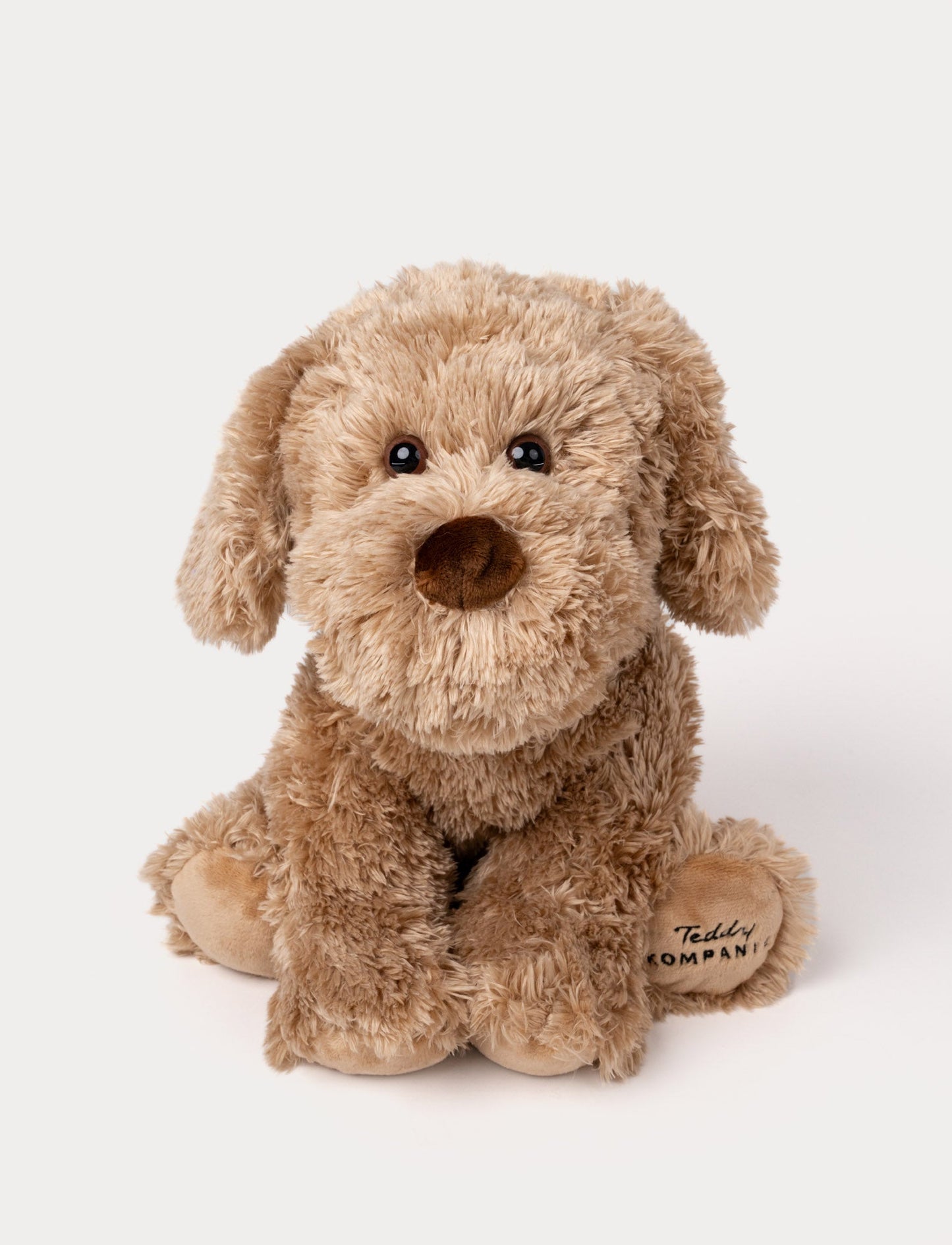 Soft, plush dog with light brown fluffy fur, black button eyes, a brown nose, and embroidered text on one paw.