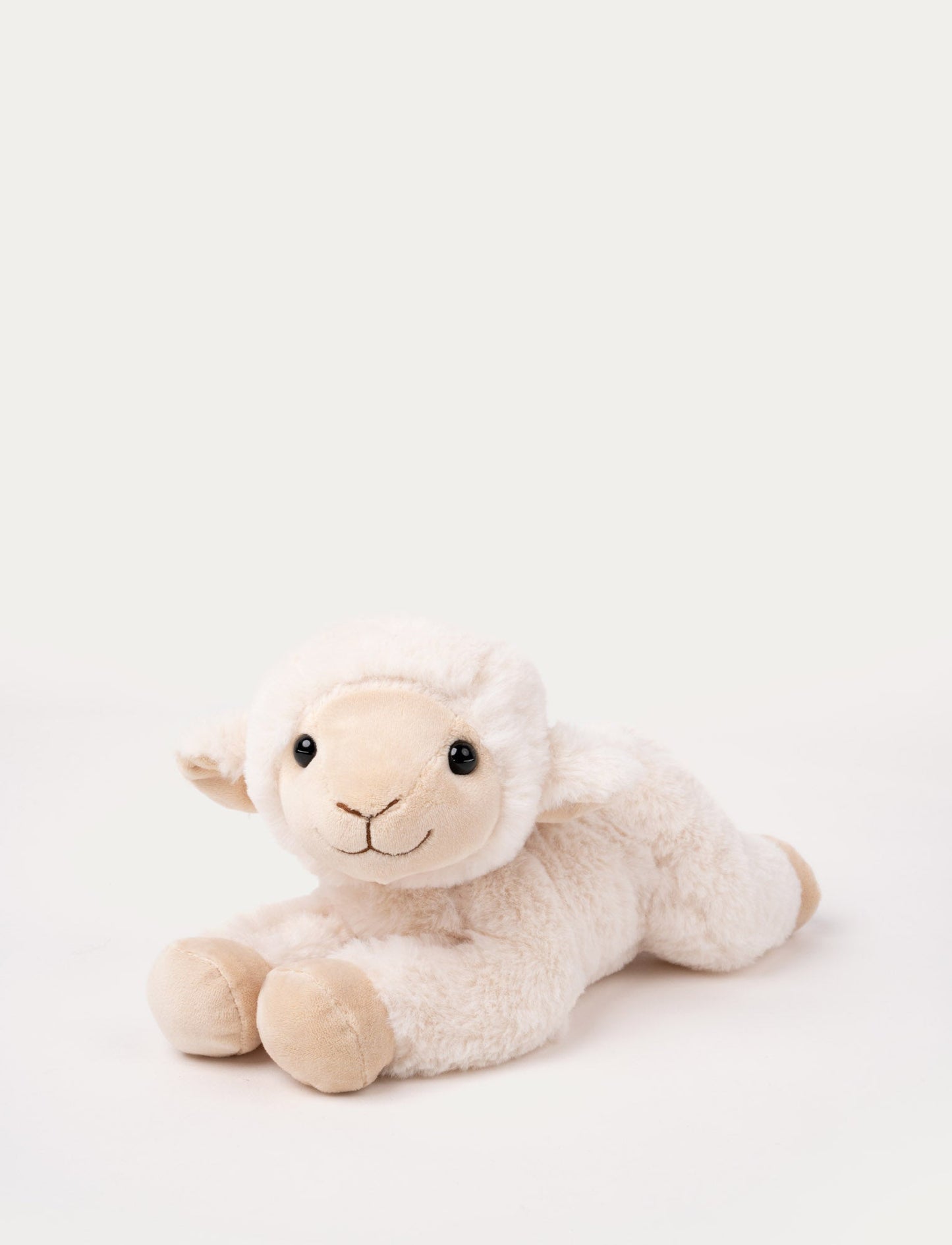 Soft plush lamb with cream-colored fur, black bead eyes, and a stitched smile, lying down.
