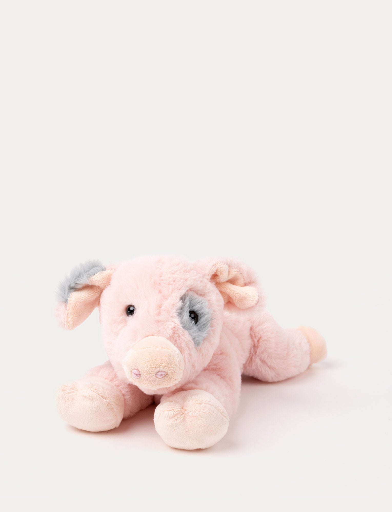  Image of Soft plush pig with pink fur, a grey patch around one eye, floppy ears, and a curled tail, lying down.