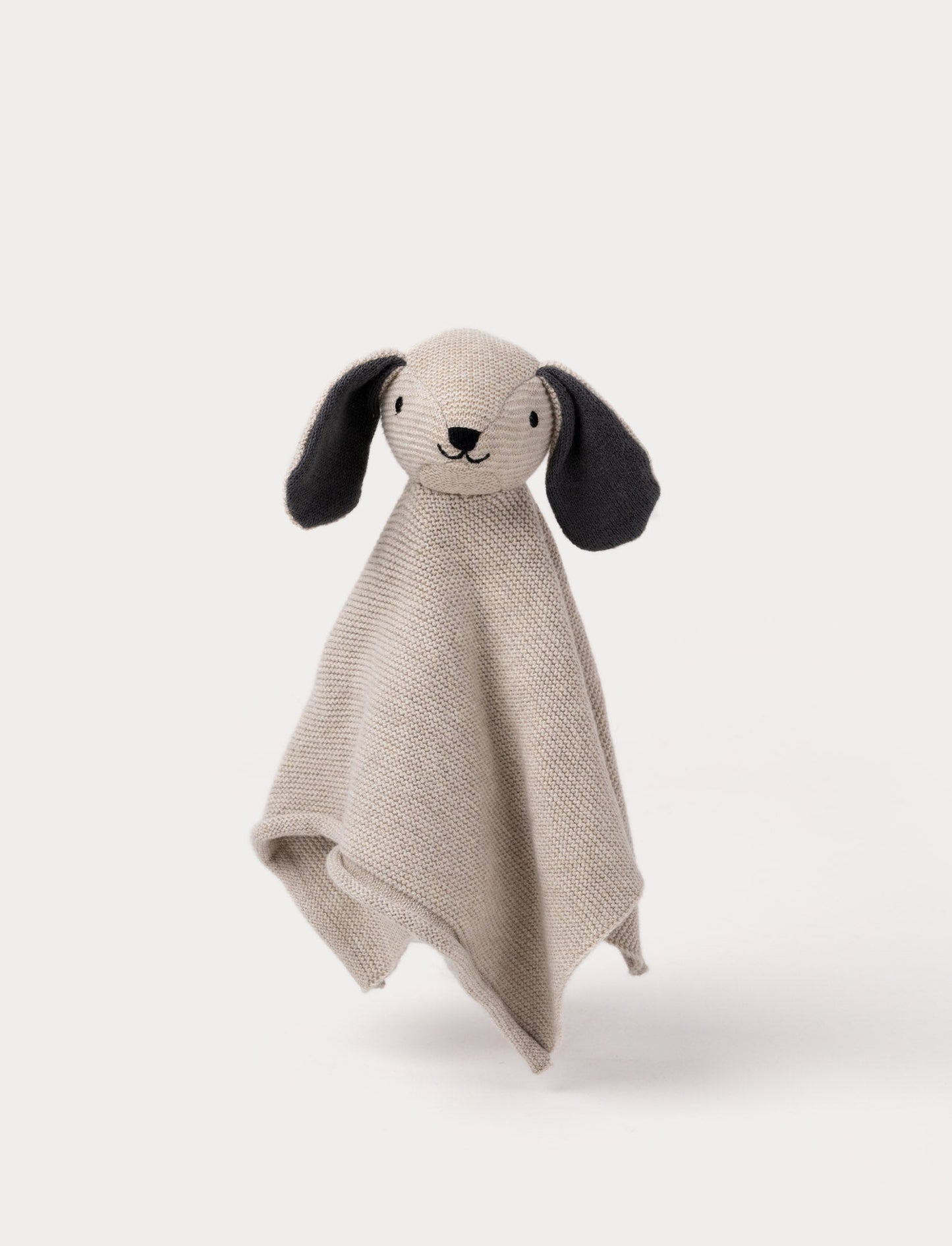 A knitted beige dog comforter with dark floppy ears, a stitched smiling face, and a soft textured fabric.