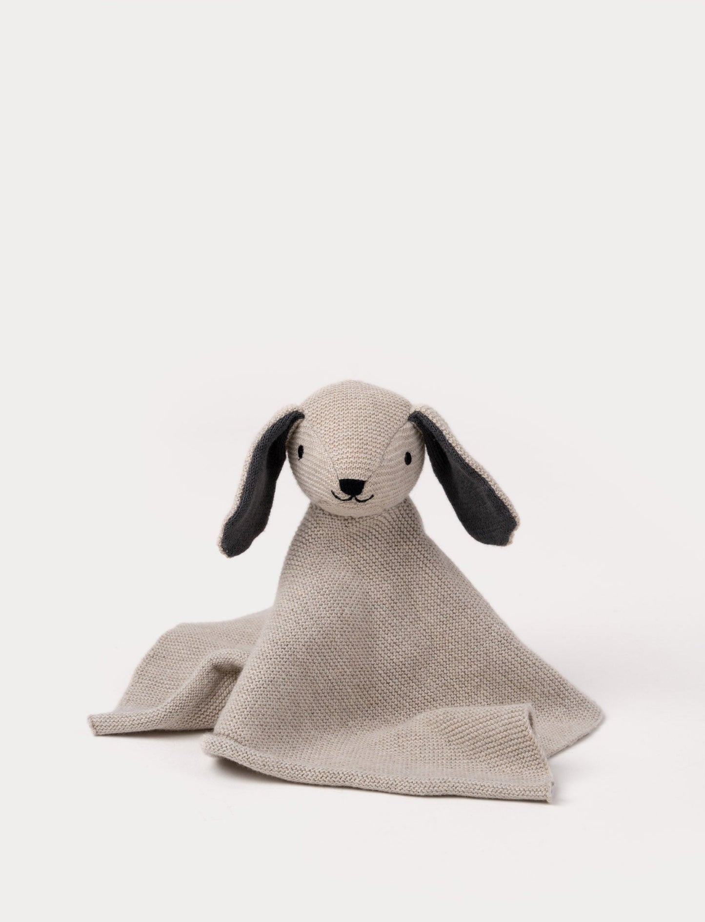 A knitted beige dog comforter with dark floppy ears, a stitched smiling face, and a soft textured fabric.