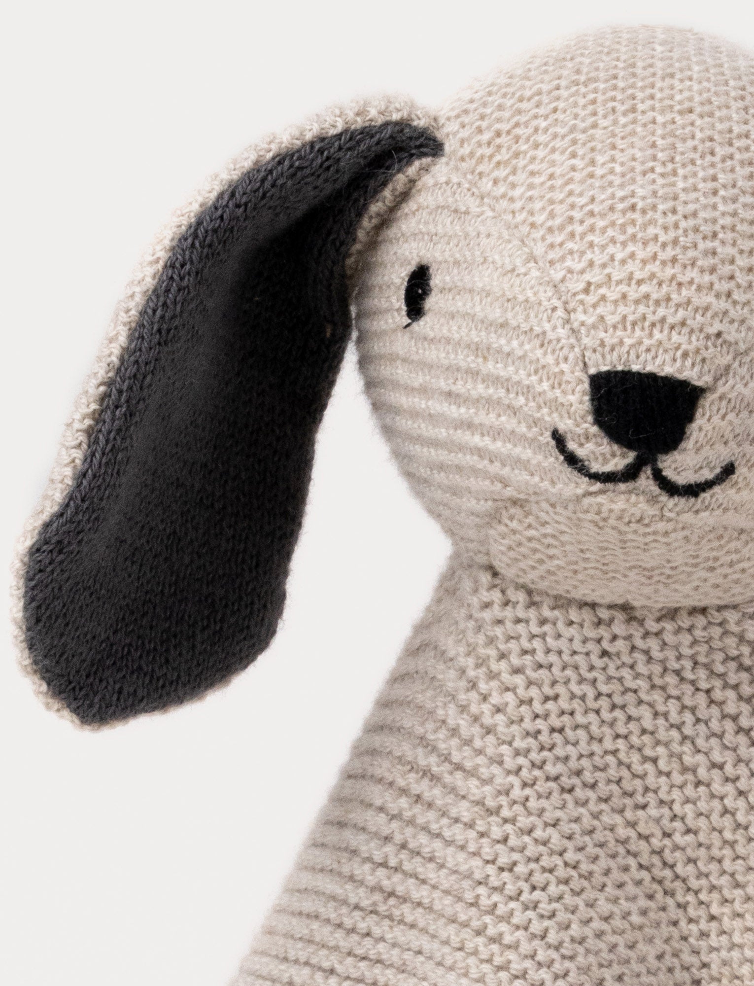  Image of A knitted beige dog comforter with dark floppy ears, a stitched smiling face, and a soft textured fabric.