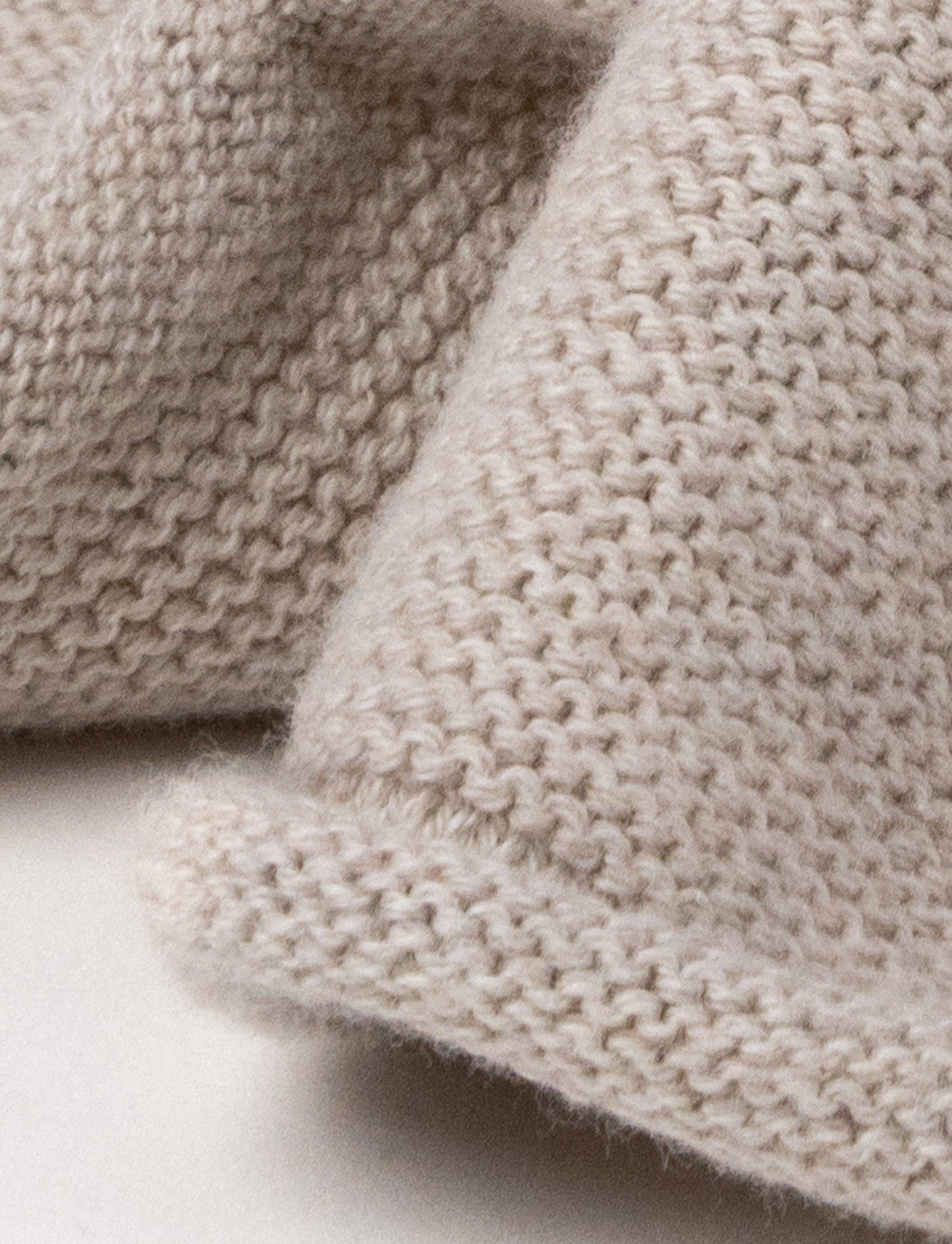 A knitted beige dog comforter with dark floppy ears, a stitched smiling face, and a soft textured fabric.