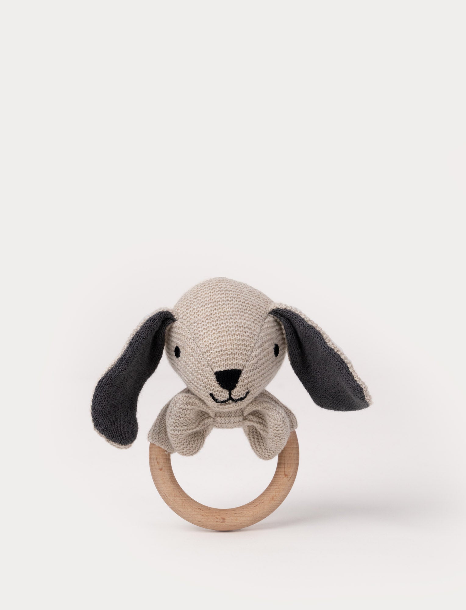  Image of Knitted beige bunny teething ring with dark floppy ears, embroidered facial features, a bow, and a smooth wooden handle.