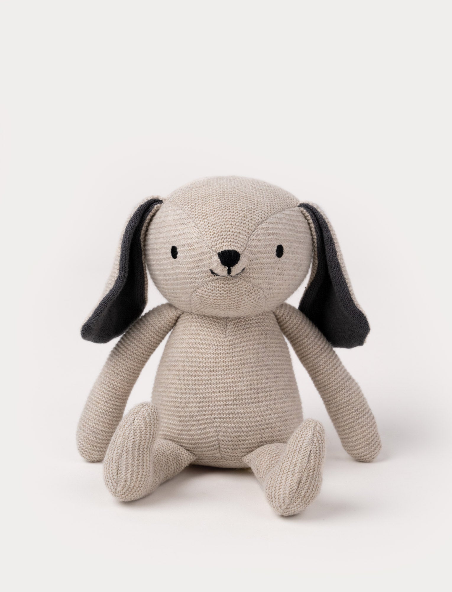  Image of A knitted beige plush dog with dark floppy ears, a stitched smiling face, and a soft textured body.