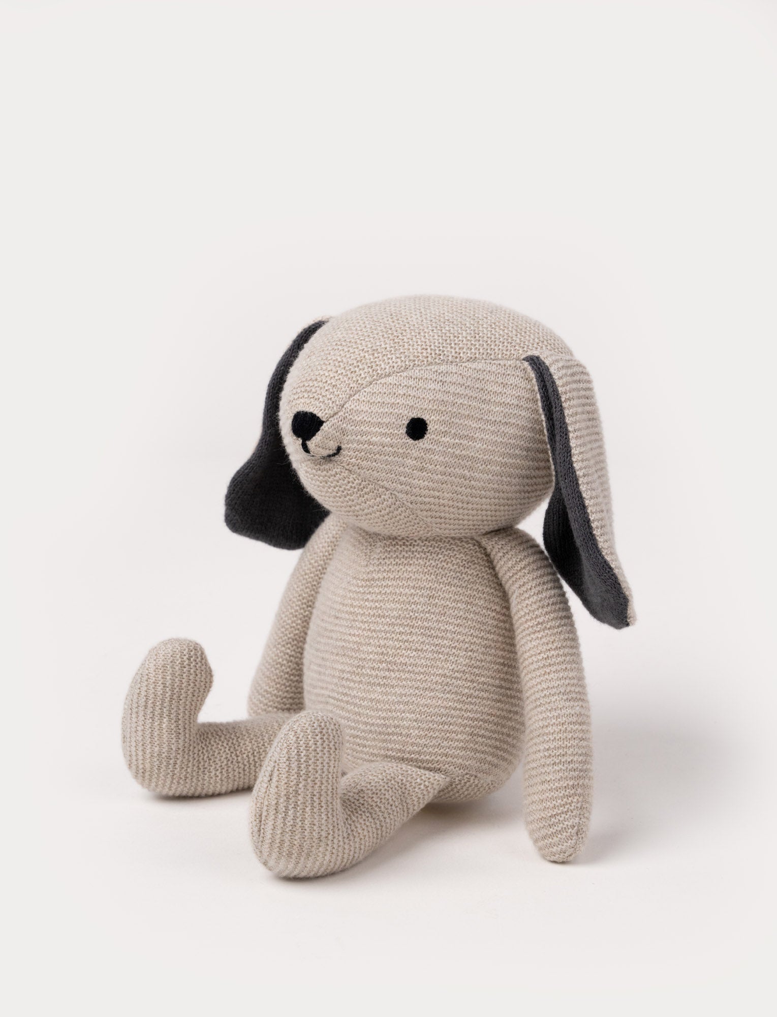  Image of A knitted beige plush dog with dark floppy ears, a stitched smiling face, and a soft textured body.