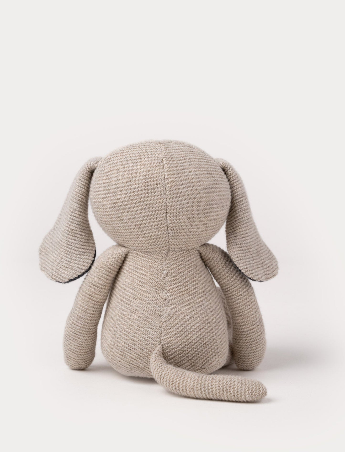 A knitted beige plush dog with dark floppy ears, a stitched smiling face, and a soft textured body.