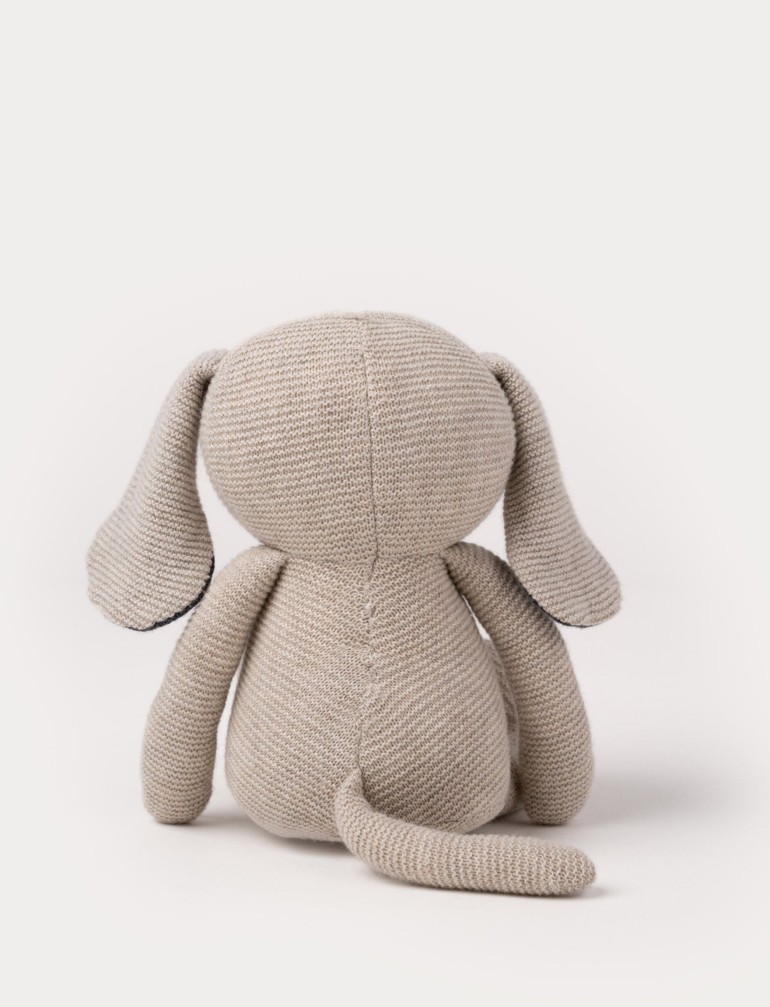  Image of A knitted beige plush dog with dark floppy ears, a stitched smiling face, and a soft textured body.