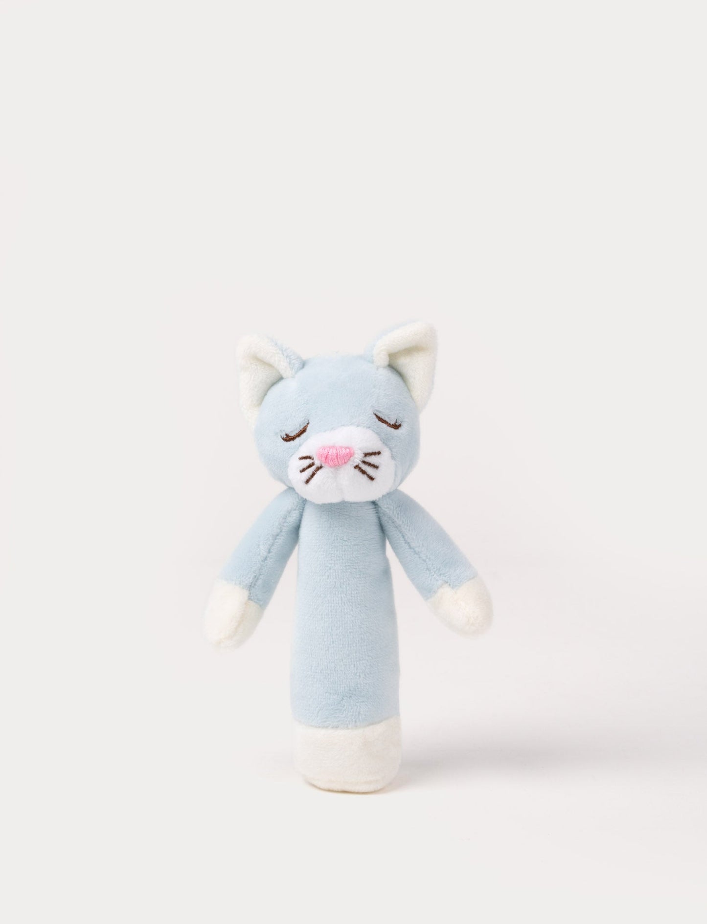 Soft plush cat rattle with a light blue body, embroidered sleeping eyes, a white muzzle, and white accents on the hands and base.